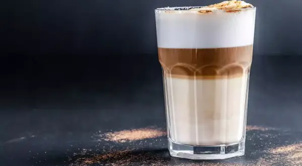 Un bicchiere di latte macchiato con strati distinti di latte, caffè e schiuma. Ecco come si fa, un piacere visivo e gustativo.