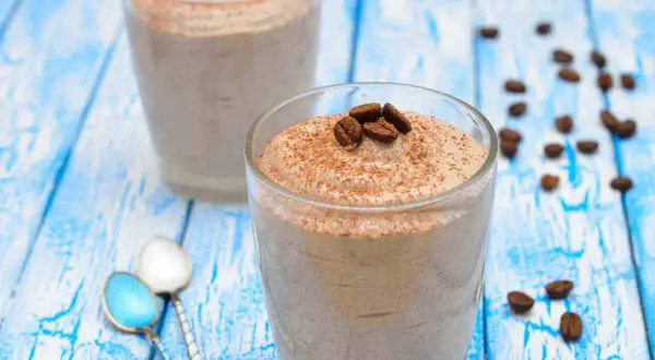Delizioso sorbetto al caffè ricetta, guarnito con chicchi di caffè e cacao, servito in bicchieri su un tavolo di legno blu.