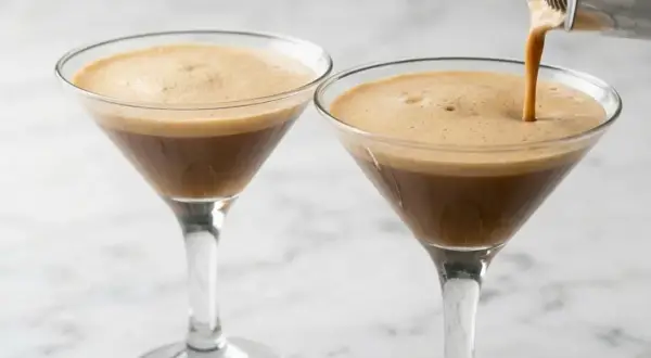 Due bicchieri di caffè shakerato cremoso, uno viene riempito da uno shaker.