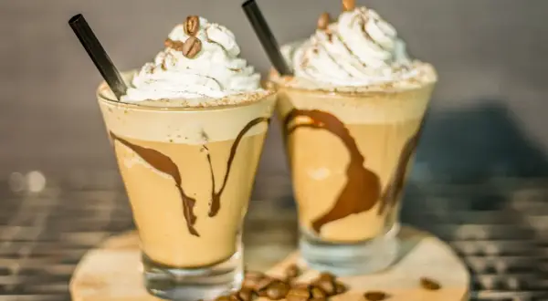 Due deliziosi milkshake al caffè, guarniti con panna montata, chicchi di caffè e sciroppo al cioccolato, pronti per essere gustati.