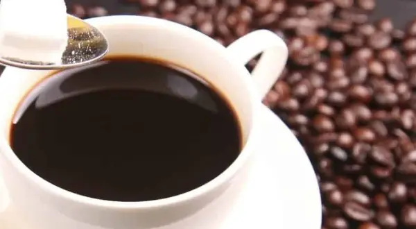 Tazza di caffè decaffeinato, chicchi tostati e zolletta di zucchero su cucchiaino. Ideale per chi vuole godersi il gusto senza preoccuparsi della pressione.