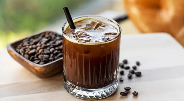 Un bicchiere di caffè freddo, con ghiaccio e cannuccia, accanto a chicchi di caffè. Ecco cos'è il cold brew: una bevanda rinfrescante.