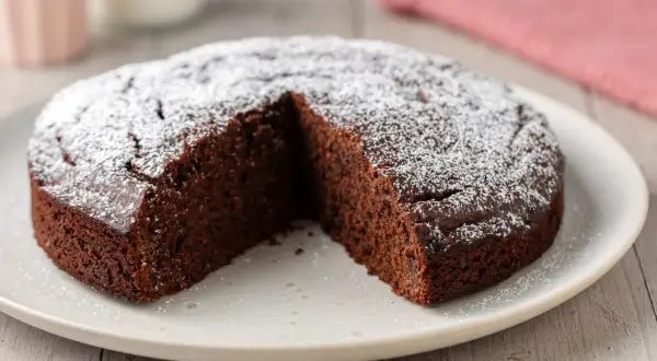 Una deliziosa torta caffè e cioccolato fondente, cosparsa di zucchero a velo, con una fetta mancante.