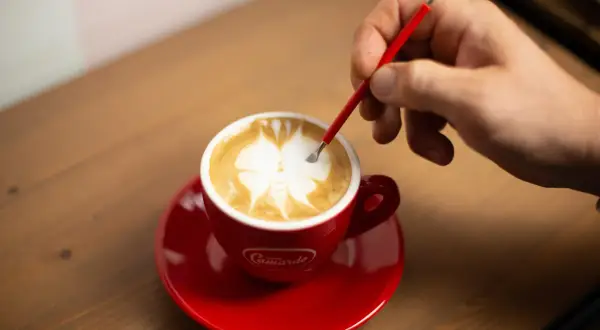 Un barista crea disegni sul cappuccino con uno strumento, mostrando come fare latte art.