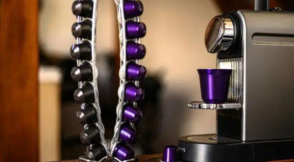 Macchina caffè Caffitaly con spia rossa lampeggiante. Capsule nere e viola in un portacapsule accanto.