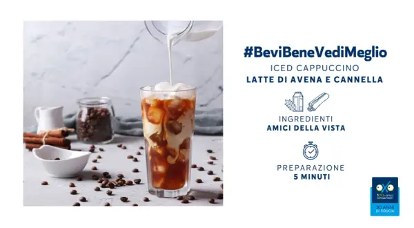 Un rinfrescante cappuccino di avena freddo versato in un bicchiere con ghiaccio, circondato da chicchi di caffè e cannella.