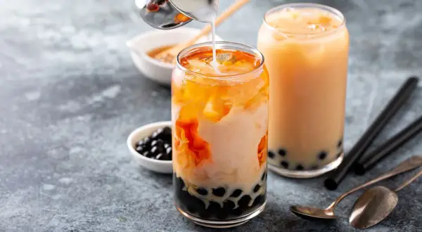 Due bicchieri di bubble tea con perle di tapioca. Un bicchiere è in preparazione con latte versato su un tè arancione.