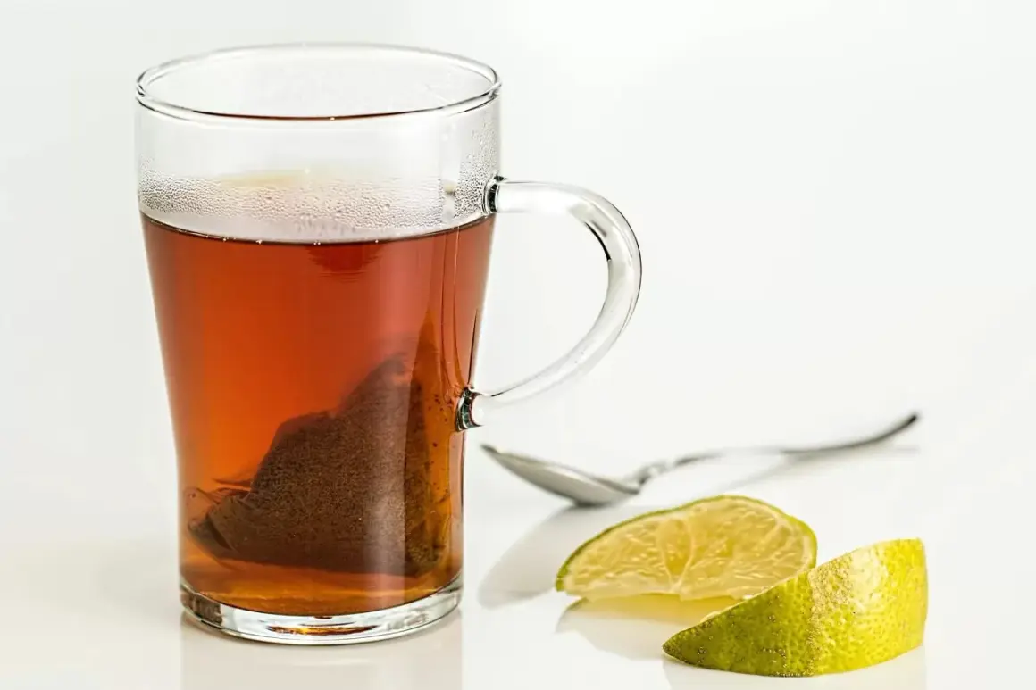 Tè caldo in tazza di vetro con bustina, limone e cucchiaino. Scopri i tè al limone benefici per il tuo benessere.