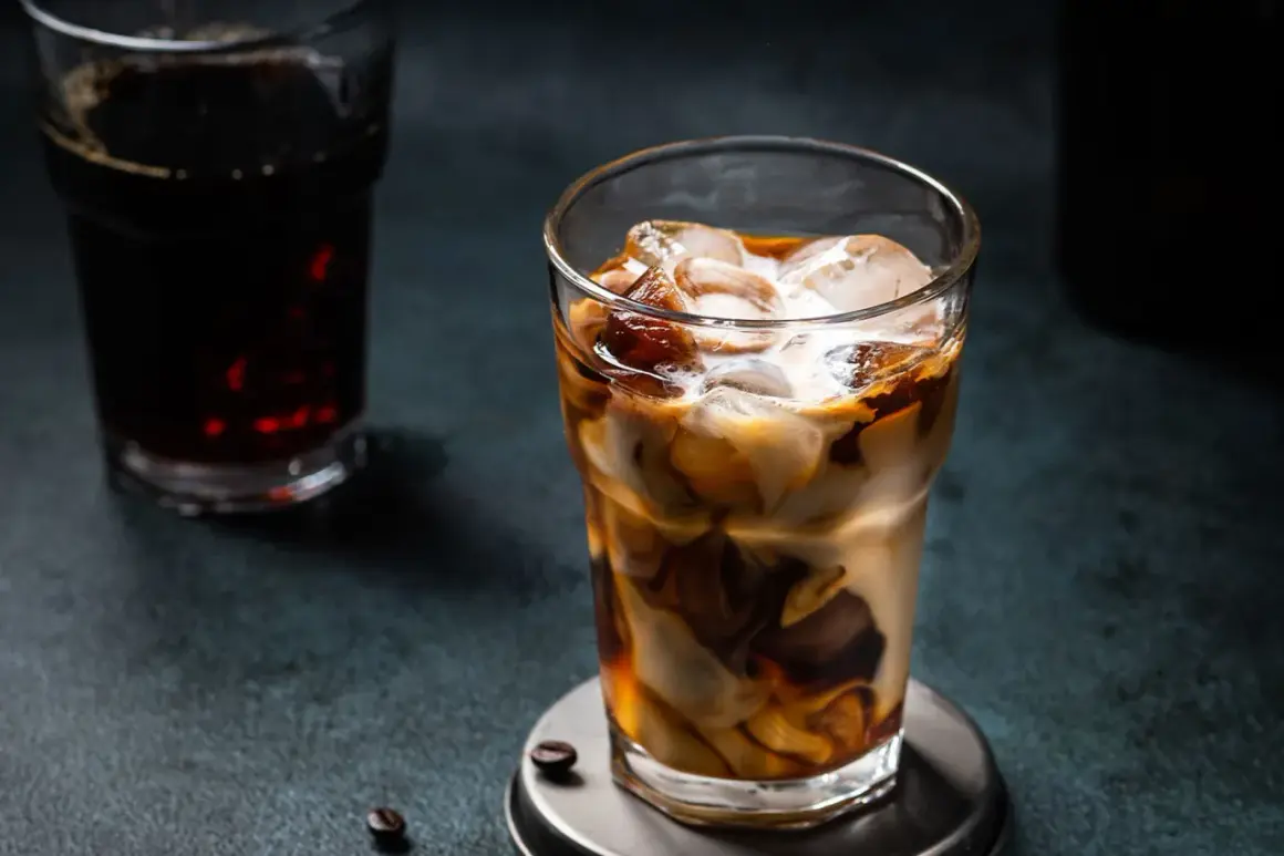 Un bicchiere di **cold brew latte** con ghiaccio, latte e caffè che si mescolano creando un effetto marmorizzato. Sullo sfondo, un altro bicchiere di caffè scuro.