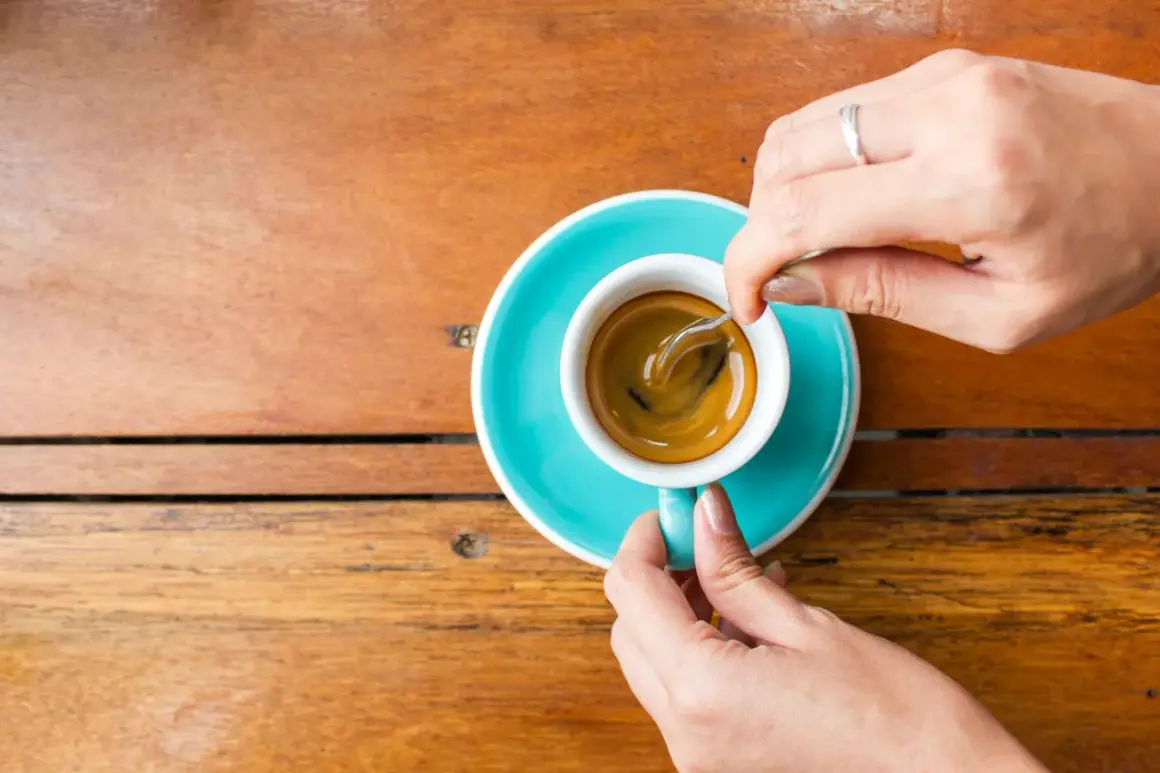 Mani che mescolano un caffè, nonostante si dica che il caffè è cancerogeno, la tazzina turchese su un tavolo di legno è invitante.