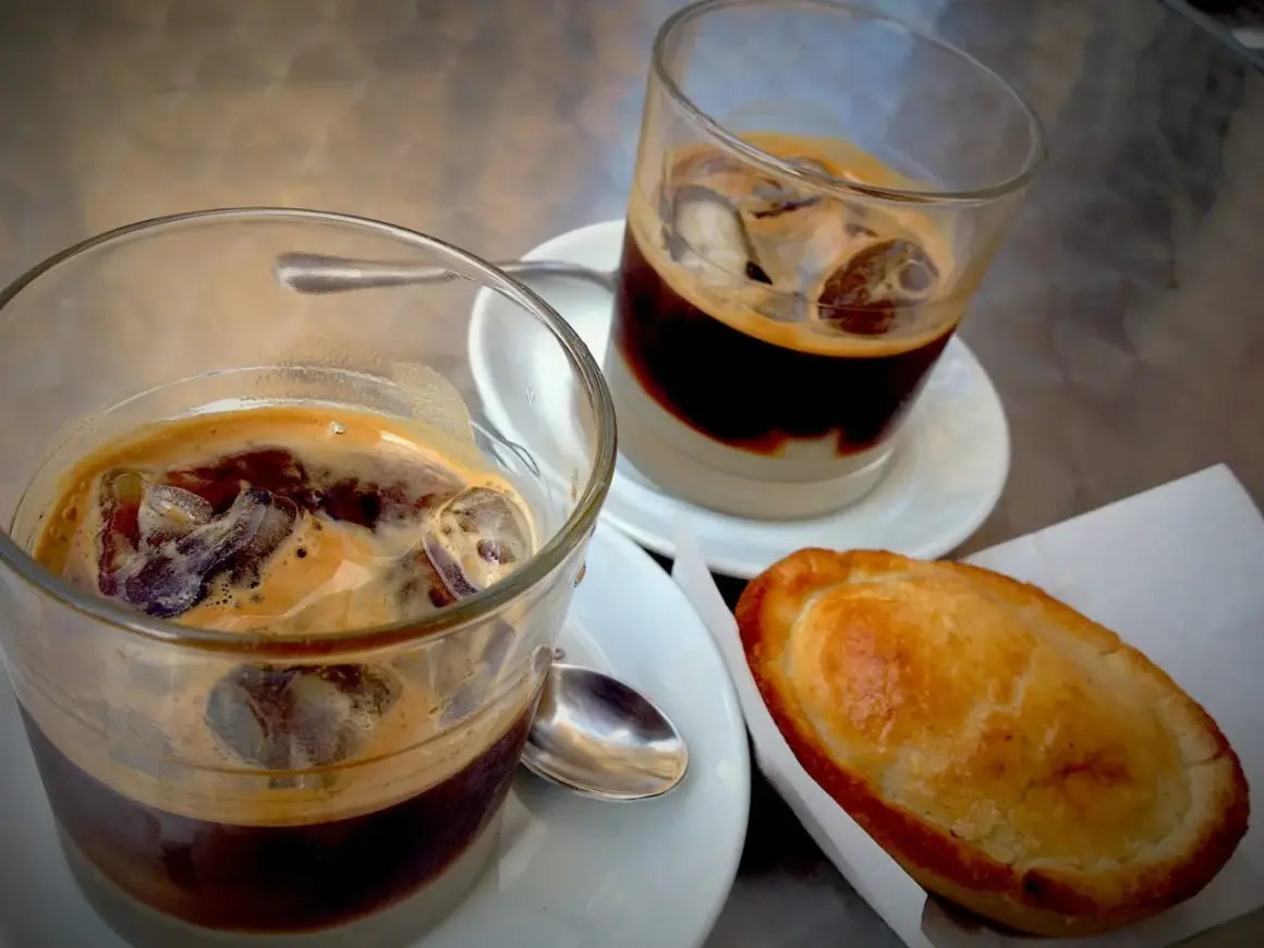 Due caffè salentino con ghiaccio e una pastarella su un tavolino.