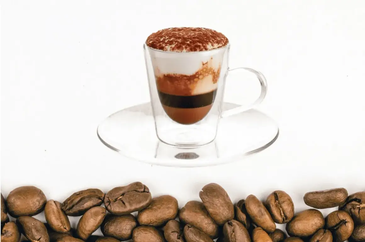 Un bicerin coffee a strati in una tazza di vetro, con cacao in polvere in cima e chicchi di caffè tostati sul fondo.