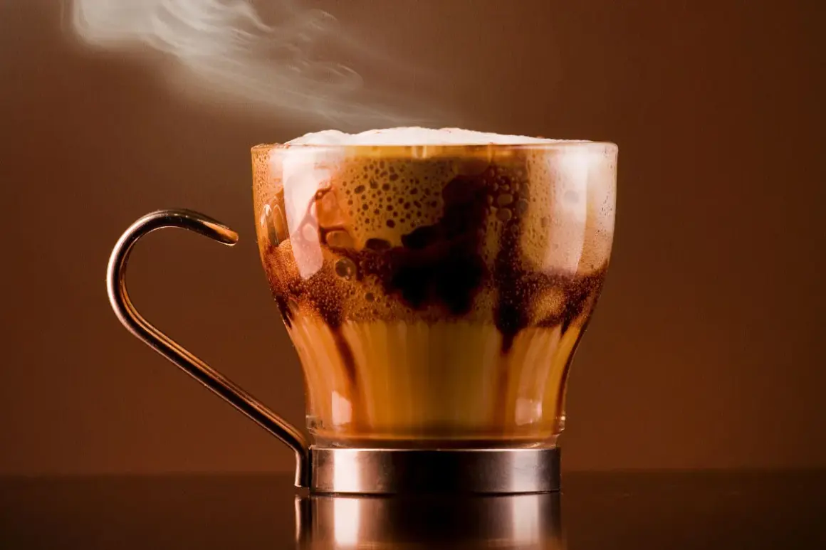 Un delizioso marocchino bevanda fumante in una tazza di vetro trasparente, con schiuma cremosa e striature di cioccolato.