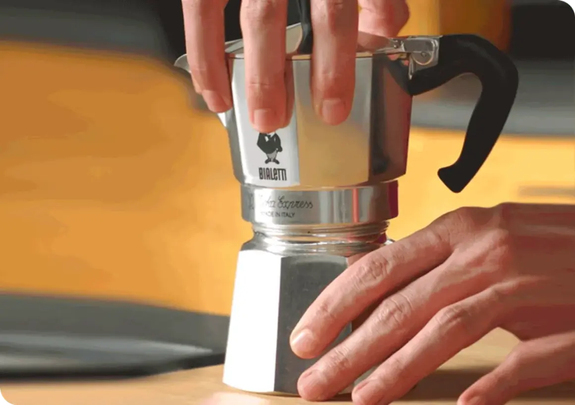 Mani che smontano una moka Bialetti per pulirla dal calcare. Un gesto semplice per un caffè perfetto.