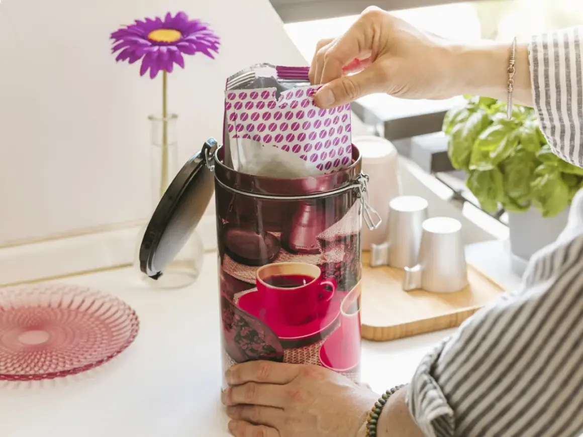 Contenitore decorato per conservare il caffè macinato, con pacchetto di caffè in mano.