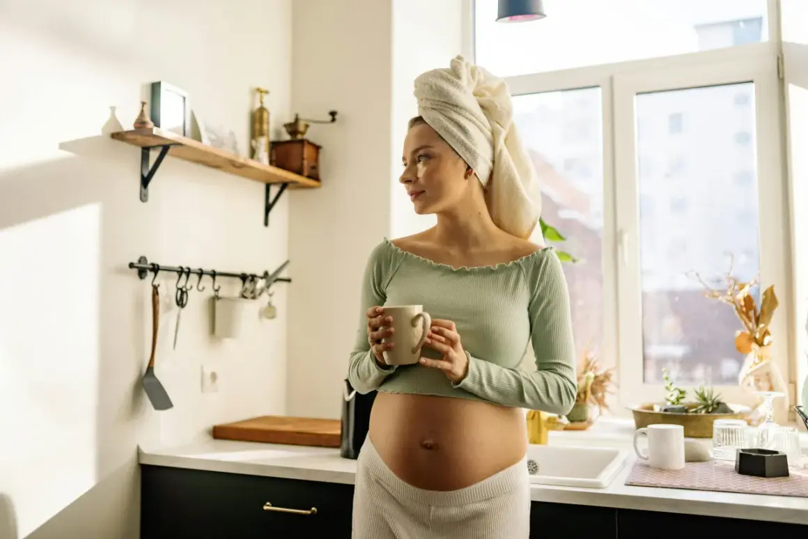 Donna incinta con asciugamano in testa beve una tisana in cucina, un momento di relax in gravidanza.