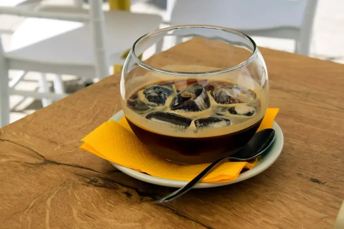 Un bicchiere di caffè freddo con ghiaccio, servito su un piattino con tovagliolo giallo e cucchiaino. Un rinfrescante caffè pugliese per una giornata calda.