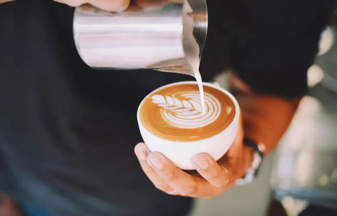 Un barista crea un disegno a latte art su un cappuccino. Latte art: cappuccino prima latte o caffè?
