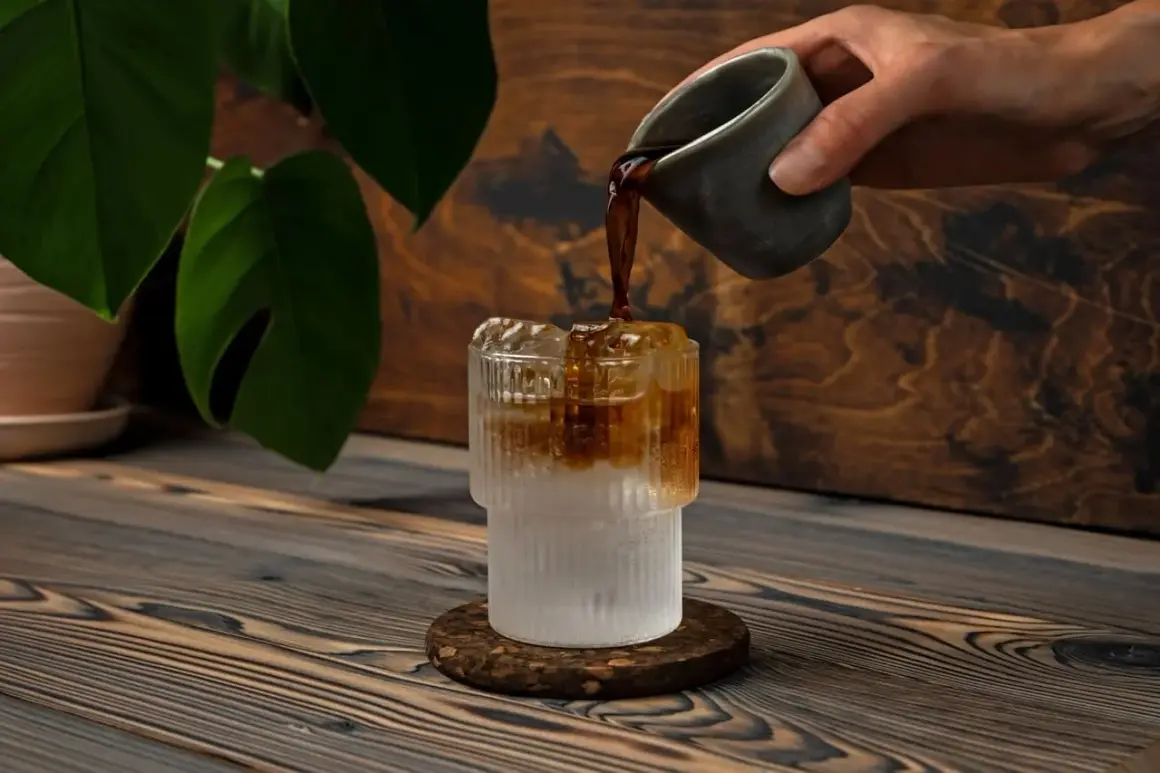 Versando caffè in un bicchiere con ghiaccio e acqua frizzante. Un'idea rinfrescante per l'estate.