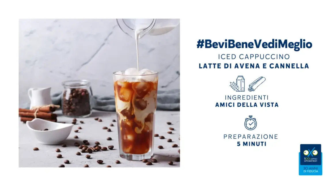 Un rinfrescante cappuccino di avena freddo versato in un bicchiere con ghiaccio, circondato da chicchi di caffè e cannella.