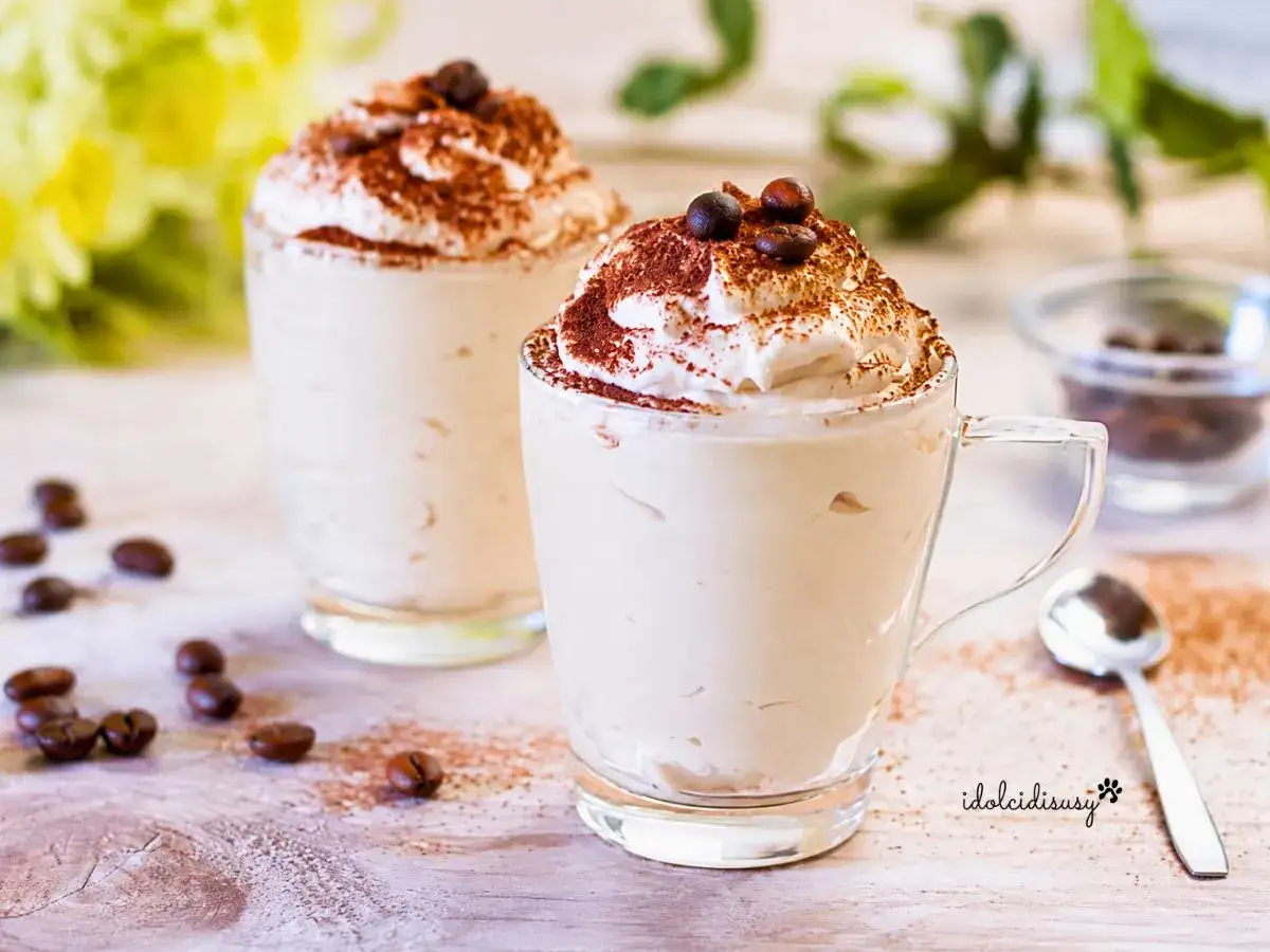Due bicchieri di deliziosa crema al caffè, guarniti con panna montata, cacao e chicchi di caffè.