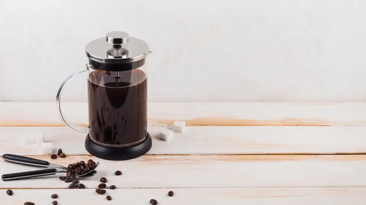Caffè francese appena preparato in una caffettiera, chicchi di caffè e zollette di zucchero su un tavolo di legno.
