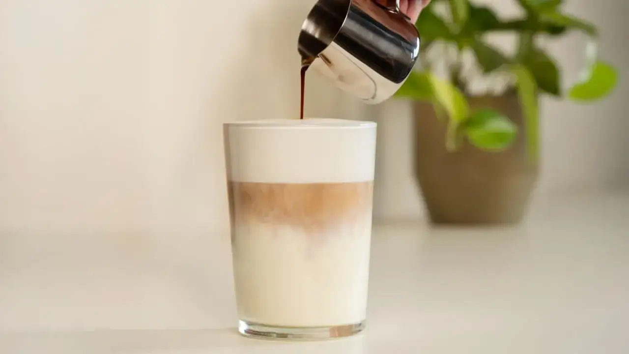 Versare caffè in un bicchiere con latte e schiuma per un perfetto latte macchiato come si fa.