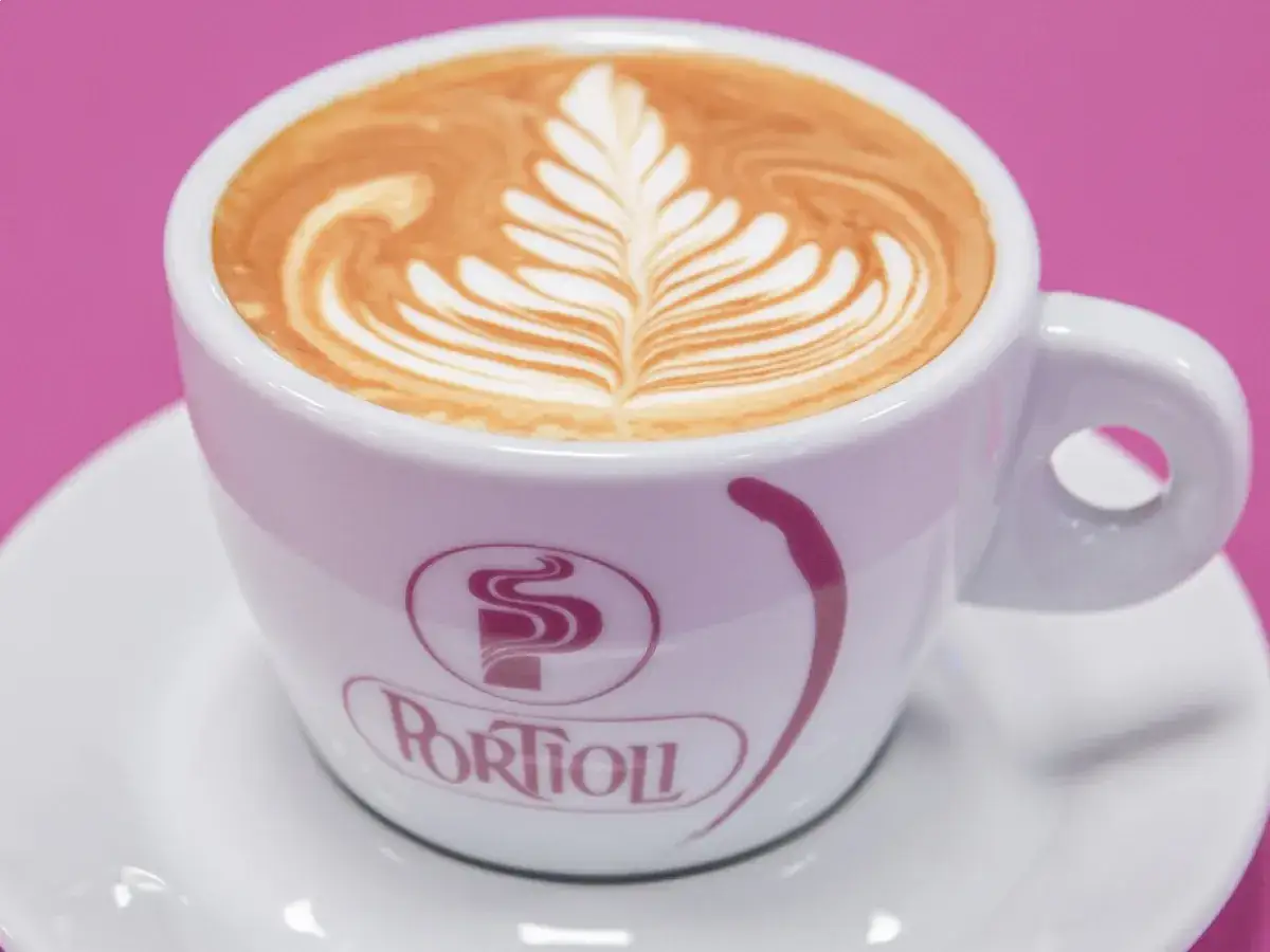 Un cappuccino con schiuma artistica, servito in una tazza bianca con logo Portioli, su un piattino.