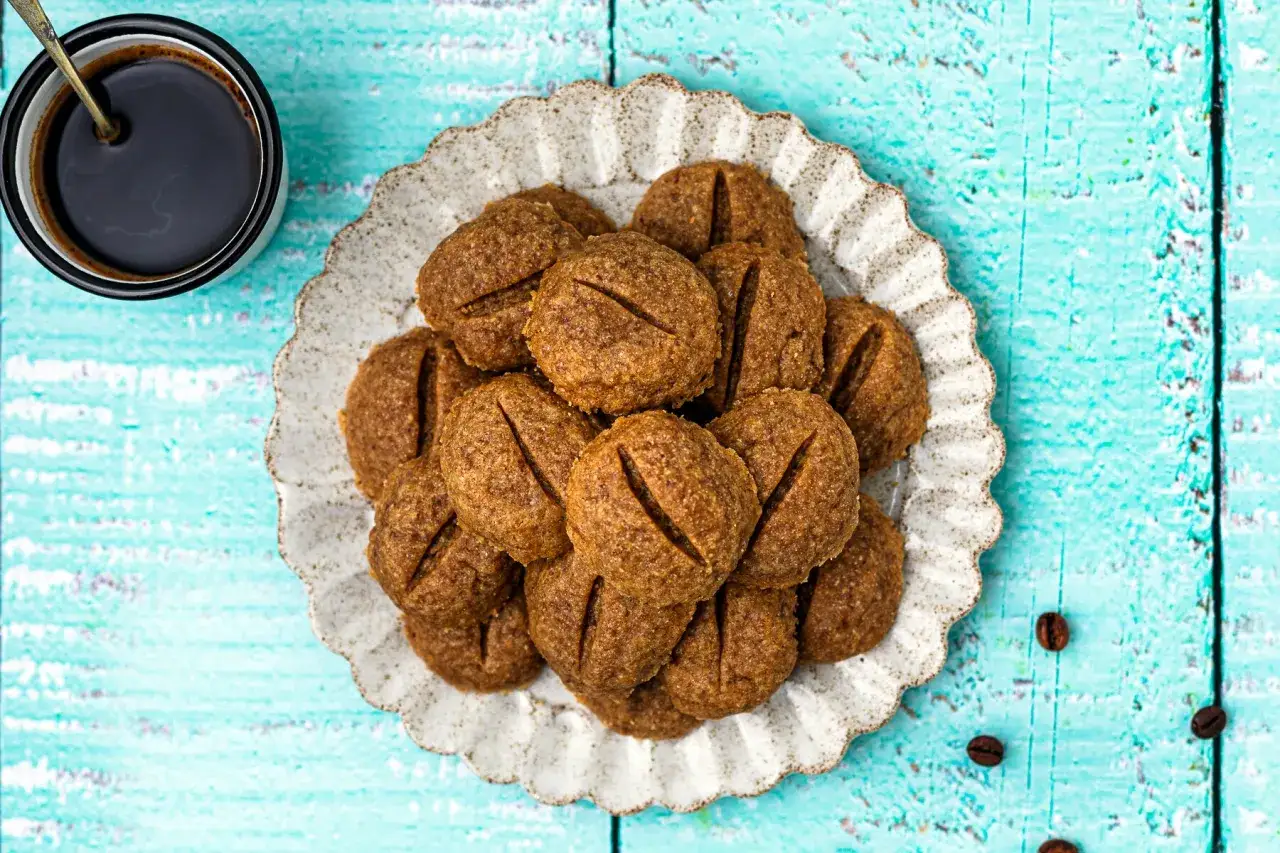 Biscotti al caffè moka su un piatto decorato, accanto a una tazzina di caffè nero. Perfetti per una pausa golosa.