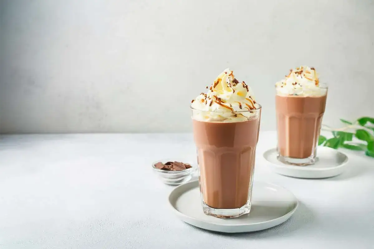 Due bicchieri di milkshake al caffè con panna montata, scaglie di cioccolato e un filo di caramello.