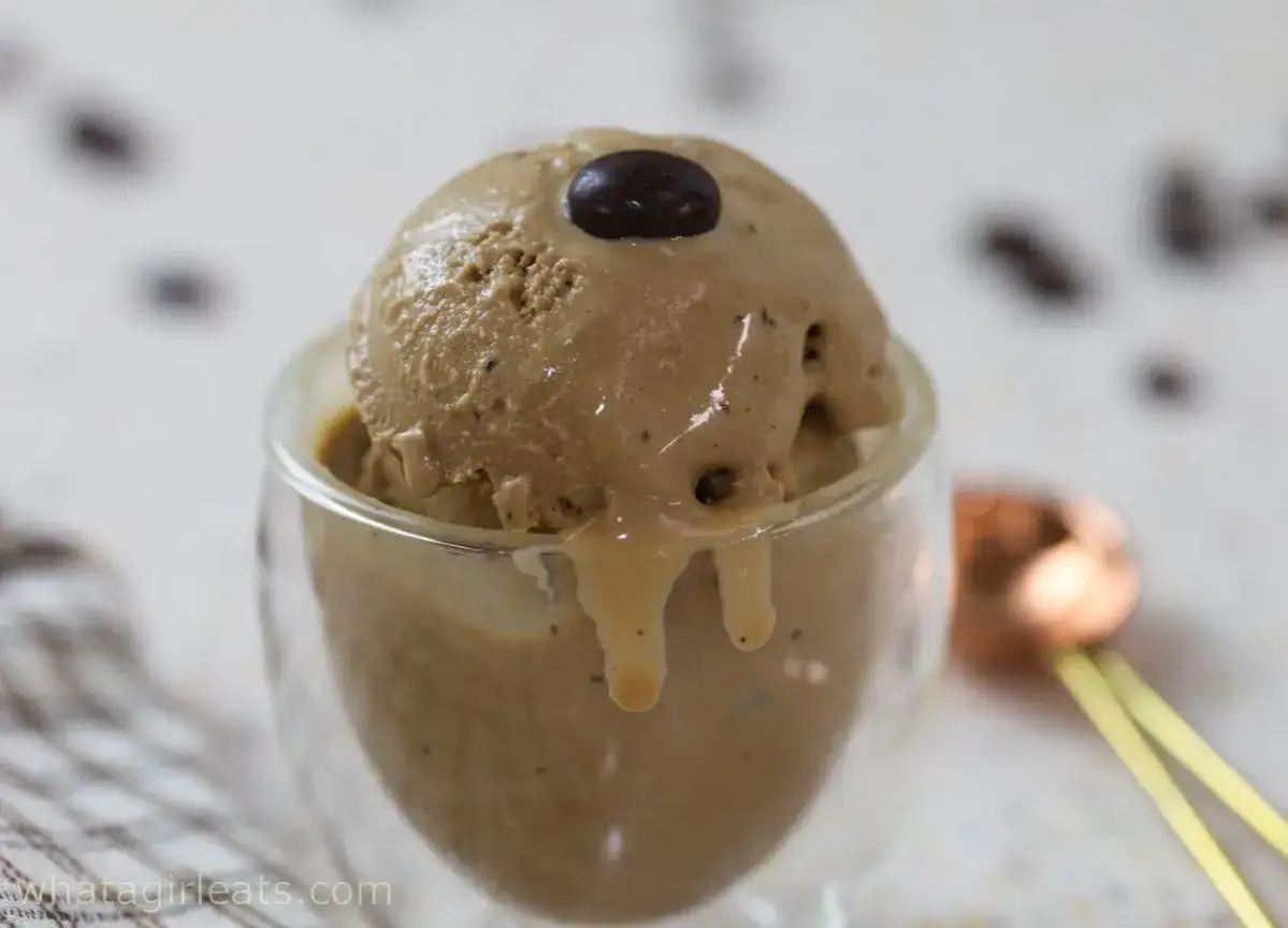 Un cremoso gelato al caffè, guarnito con un chicco scuro, si scioglie in una coppetta di vetro.