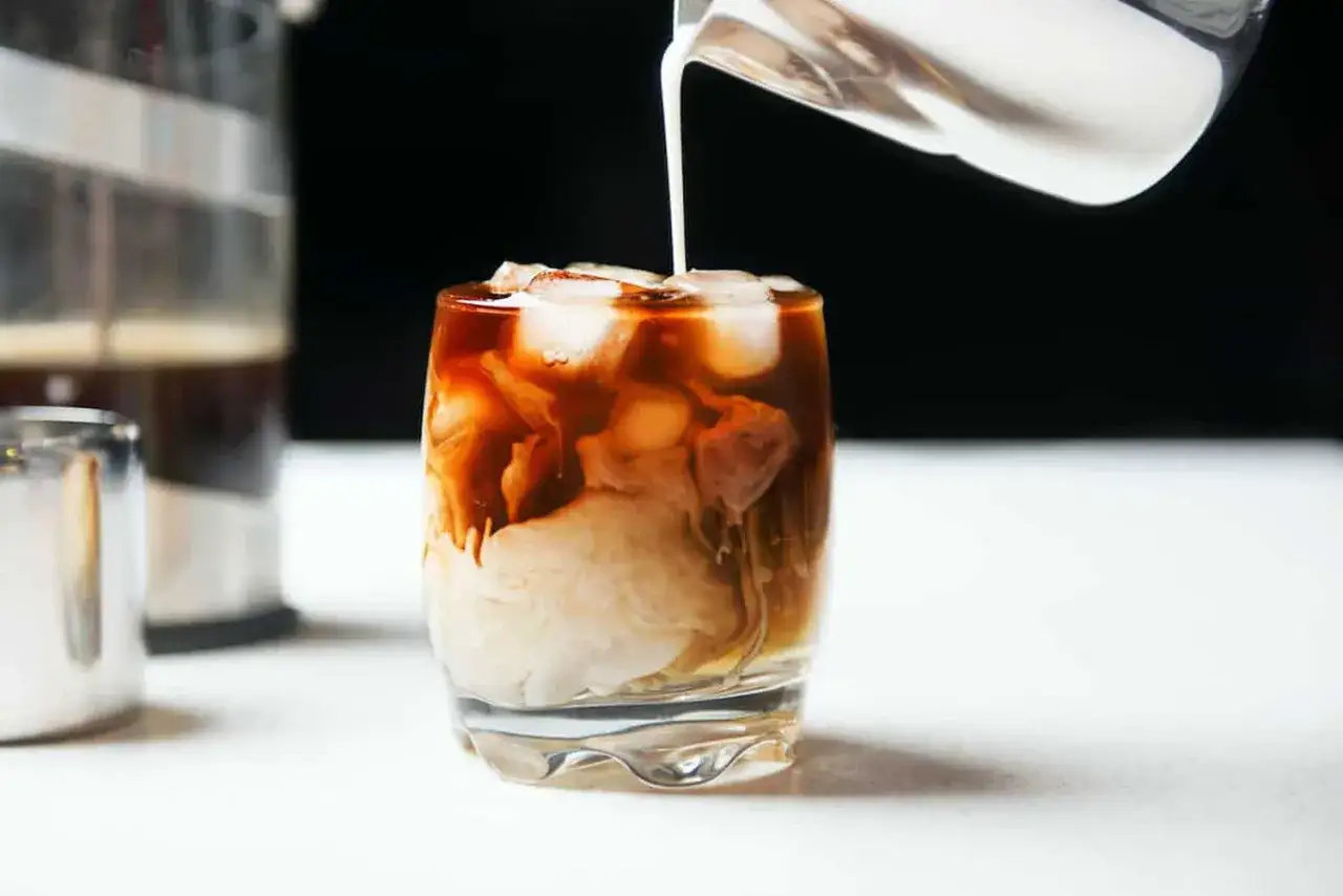 Versando latte di avena su un bicchiere di caffè freddo con ghiaccio, creando un effetto marmorizzato. Un cappuccino di avena perfetto.