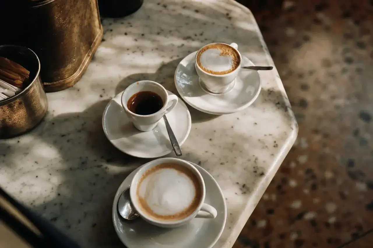 Tre tazze di italian coffees su un tavolo di marmo: un espresso intenso, un cappuccino cremoso e un altro caffè con schiuma.