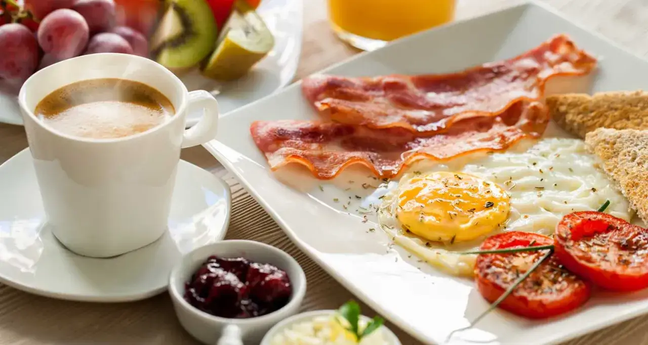 Colazione completa con caffè fumante, uova, bacon, pomodori, toast e frutta. Un inizio energico per godere dei benefici del caffè.
