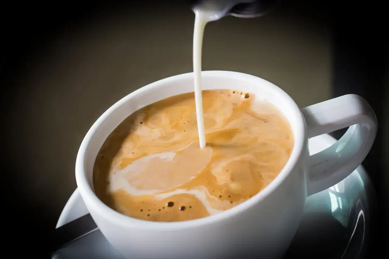 Un filo di latte si versa in un caff&egrave;, creando un cappuccino senza schiuma. La bevanda calda invita a un momento di relax.