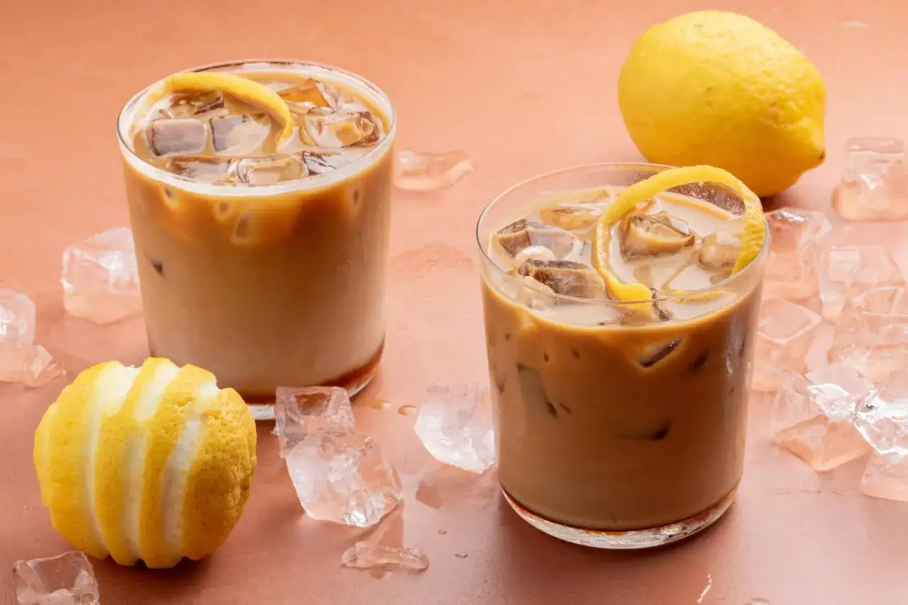 Due bicchieri di caffè con ghiaccio e scorza di limone, circondati da cubetti di ghiaccio e limoni interi. Un rinfrescante caffè con acqua frizzante.