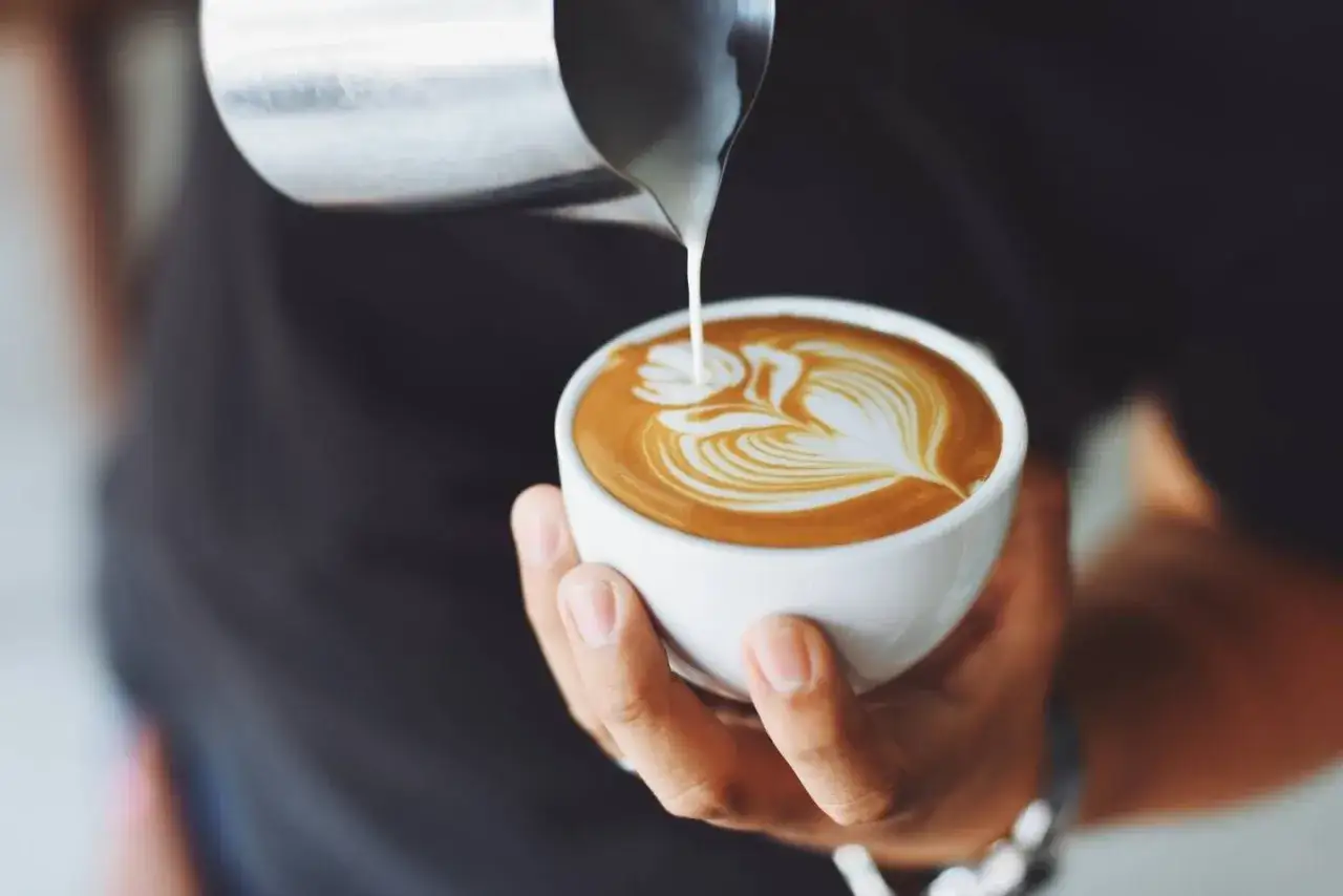 Barista versa latte art su un cappuccino, mostrando come fare il cappuccino perfetto con schiuma cremosa.