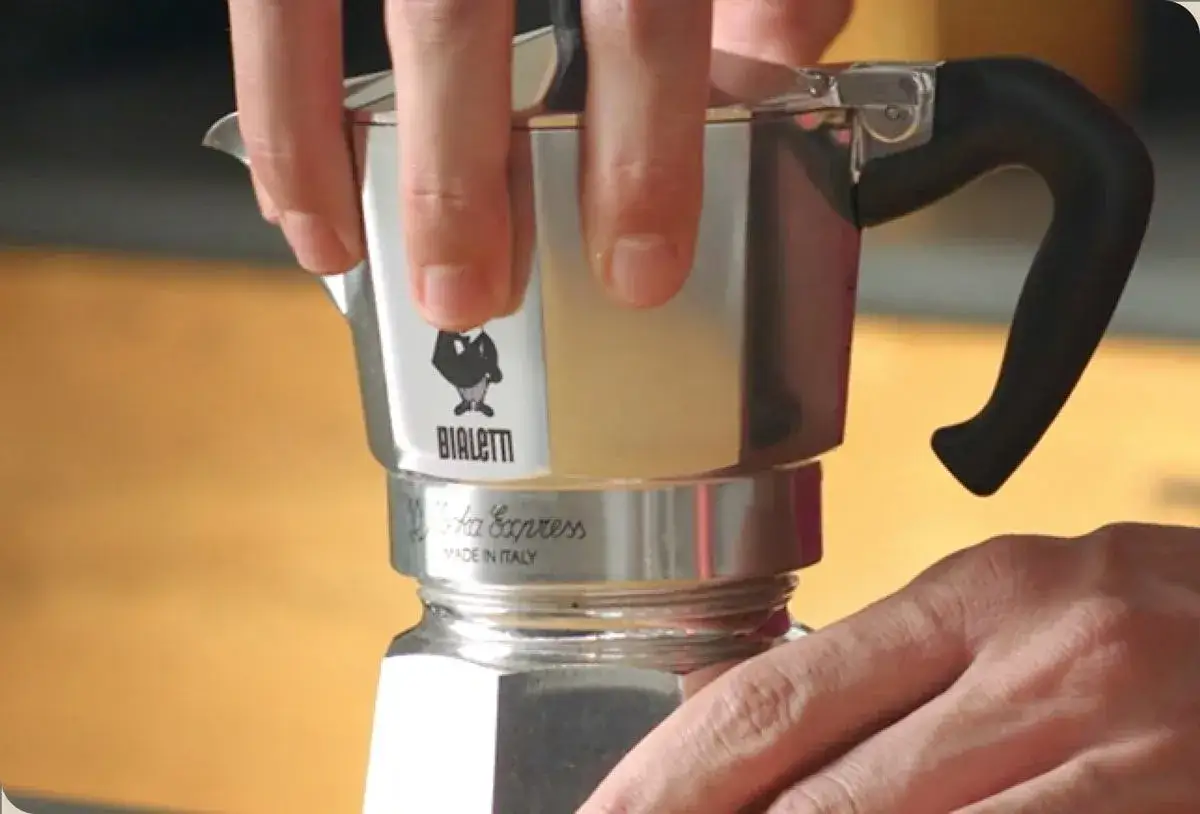 Mani che stringono una moka Bialetti. Speriamo che la caffettiera non esca caffè, altrimenti la colazione è rovinata!