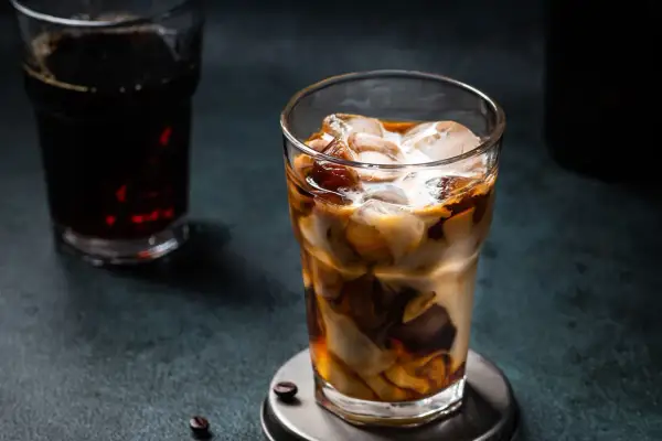 Un bicchiere di **cold brew latte** con ghiaccio, latte e caffè che si mescolano creando un effetto marmorizzato. Sullo sfondo, un altro bicchiere di caffè scuro.