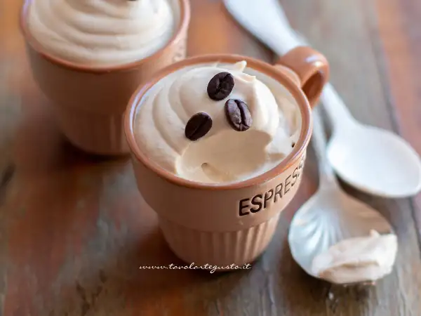 Deliziosa ricetta crema caffè con panna, guarnita con chicchi di caffè, servita in tazzine su un tavolo di legno.