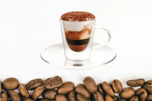 Un bicerin coffee a strati in una tazza di vetro, con cacao in polvere in cima e chicchi di caffè tostati sul fondo.