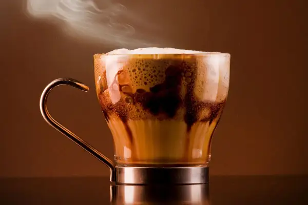 Un delizioso marocchino bevanda fumante in una tazza di vetro trasparente, con schiuma cremosa e striature di cioccolato.