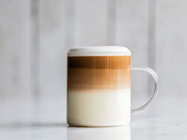 Un bicchiere di caffè macchiato caldo con strati distinti di latte e caffè, sormontato da una schiuma soffice.