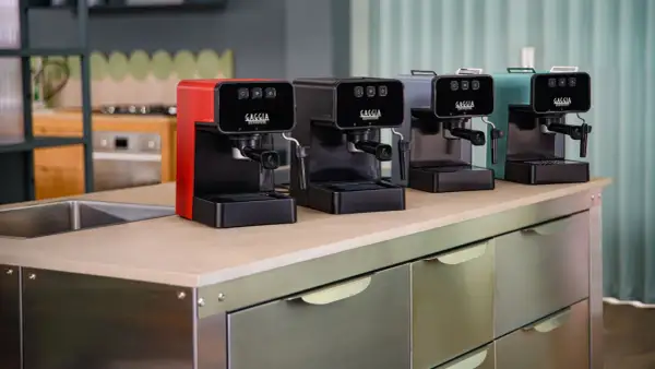 Macchine da caffè Gaggia in vari colori, una rossa, una nera, una grigia e una verde acqua, disposte su un bancone. Speriamo che la macchina caffè Gaggia non esca il caffè, altrimenti la colazione è rovinata!