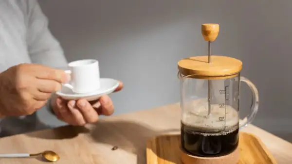 Un uomo tiene una tazzina di caffè mentre una french press caffè è pronta per essere servita.