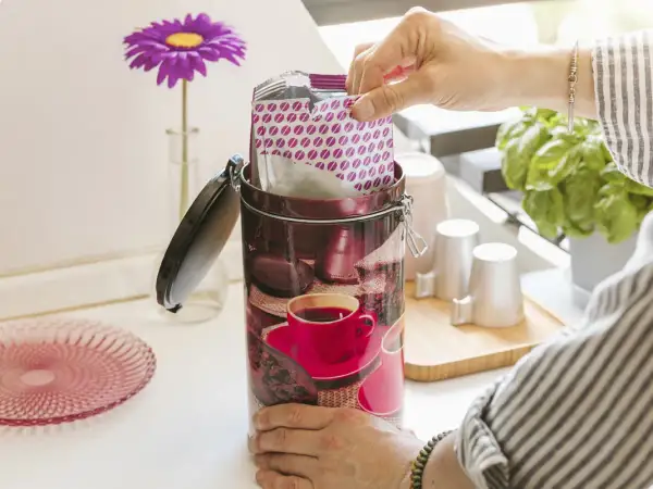 Contenitore decorato per conservare il caffè macinato, con pacchetto di caffè in mano.