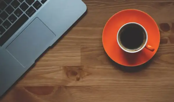 Tazza di caffè nero su piattino arancione accanto a un laptop. Scopri quando bere il caffè per dimagrire.