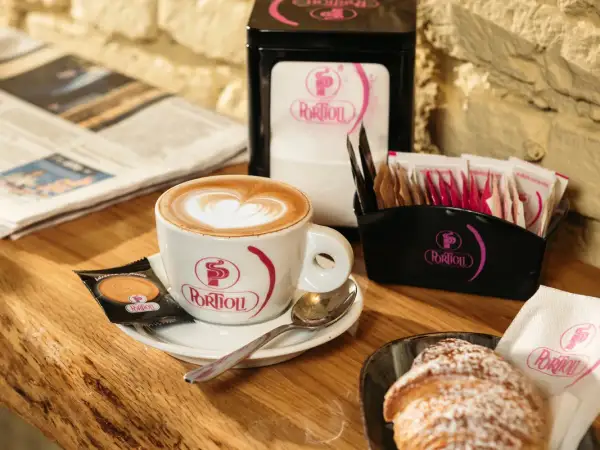 Un cappuccino perfetto con schiuma a forma di cuore, accompagnato da un croissant e un giornale.