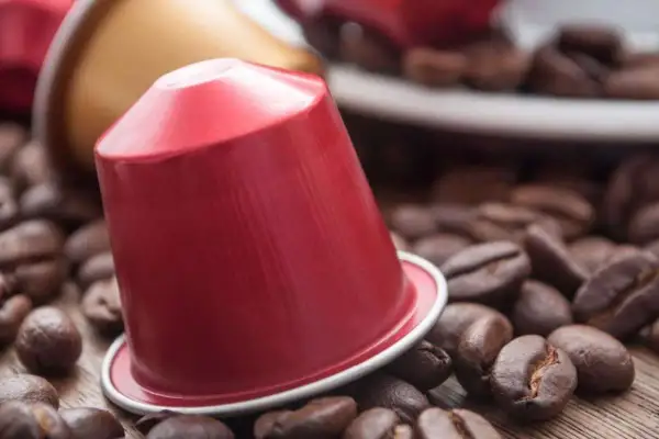 Una capsula di caffè rossa, circondata da chicchi di caffè tostati, pronta per un'esperienza aromatica.