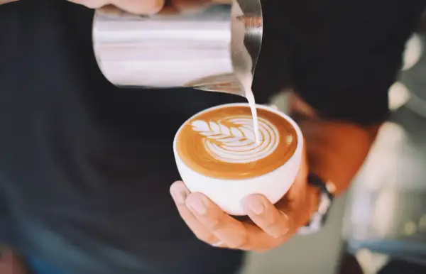 Un barista crea un disegno a latte art su un cappuccino. Latte art: cappuccino prima latte o caffè?